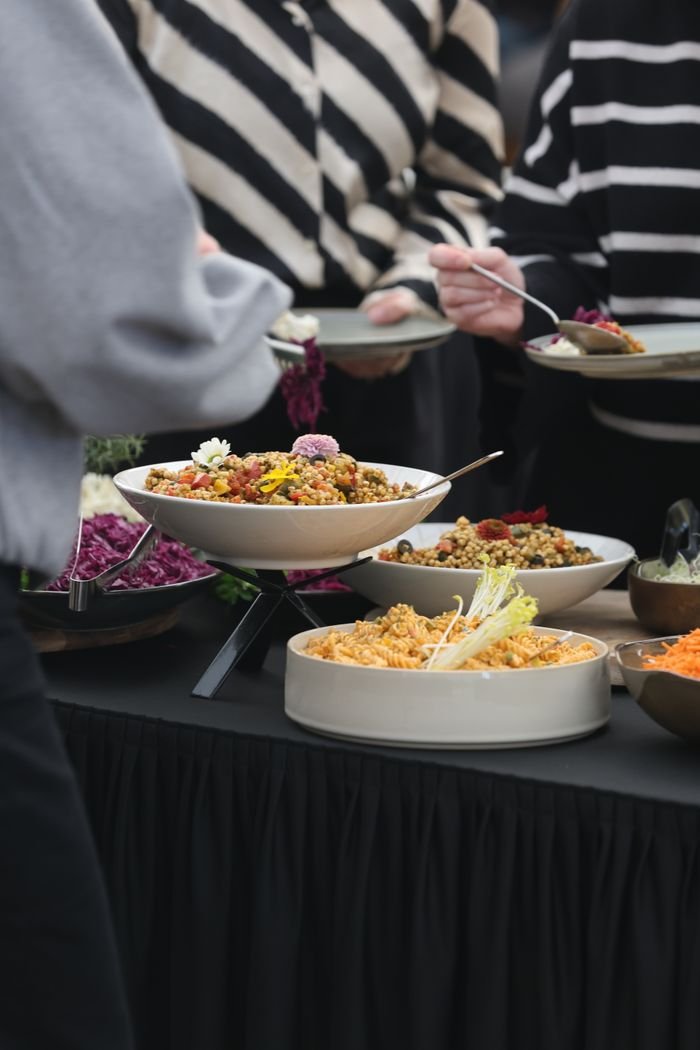 A diverse array of colorful dishes on a buffet table at a gathering, featuring salads and grains.